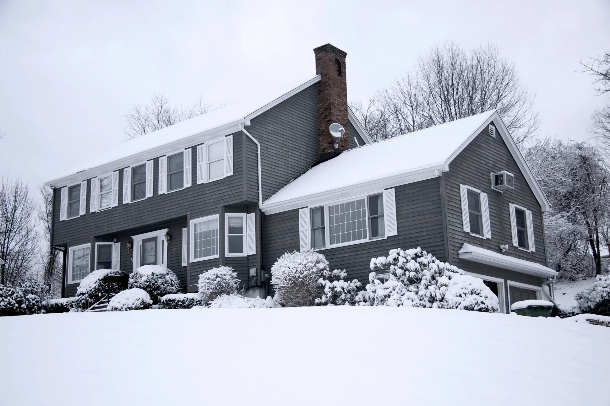 home with gray siding and snow covered roof in winter