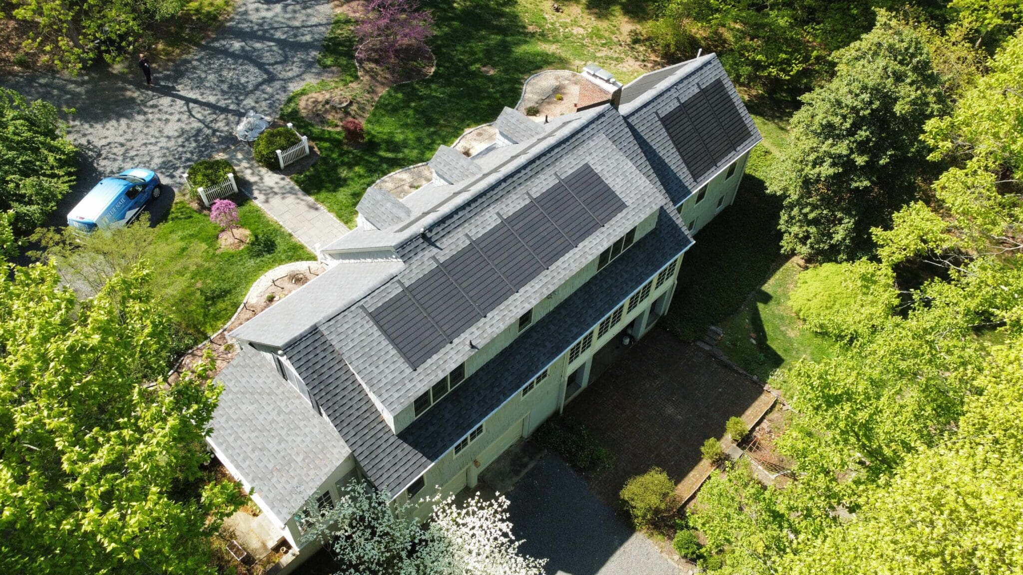 a house with gaf timberline solar shingles as roof in the spring and a driveway surrounded by trees